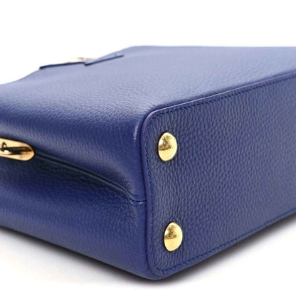 Close-up of blue handbag corner with gold-tone snap studs and pebbled texture