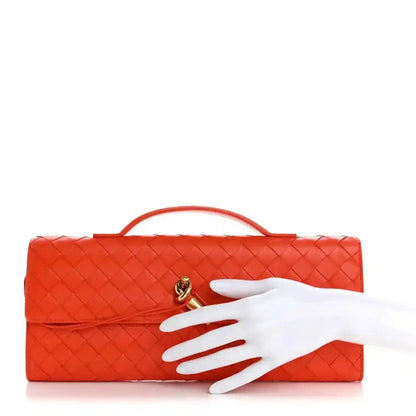Orange intrecciato nappa top handle clutch with gold-tone clasp; hand shown for scale