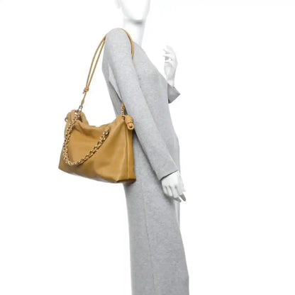 Tan leather clutch on model with chain strap draped over shoulder
