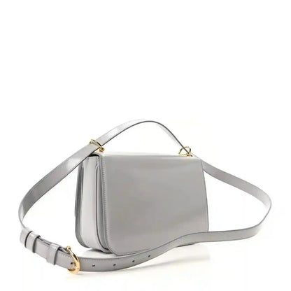 Light grey small shoulder bag with curved flap, gold-tone hardware, and crossbody strap