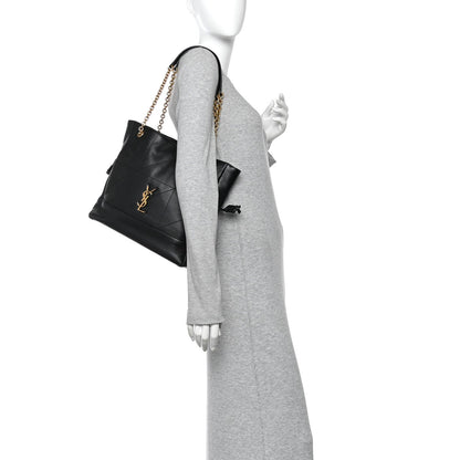 Black small shopping tote on model with gold chain strap and drawstring bow detail.