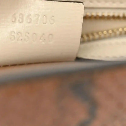 Embossed date code on light leather next to gold zipper hardware.