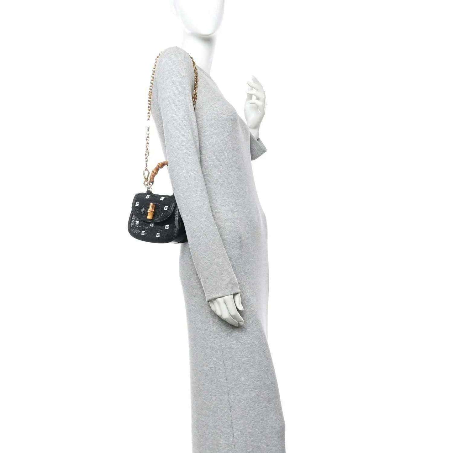 Black mini chain bag with gold chain strap, shown on a mannequin wearing a gray outfit