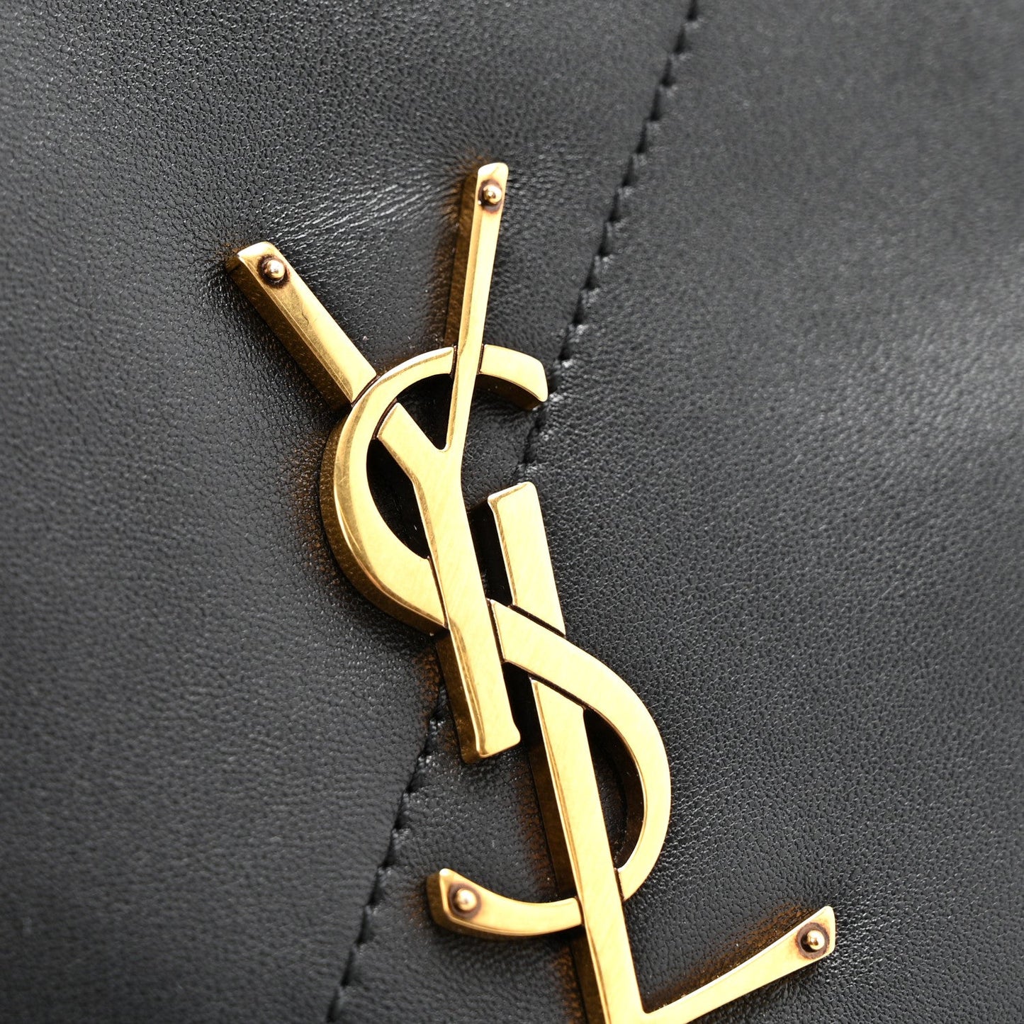 Gold YSL monogram hardware on black quilted leather bag front with stitched border