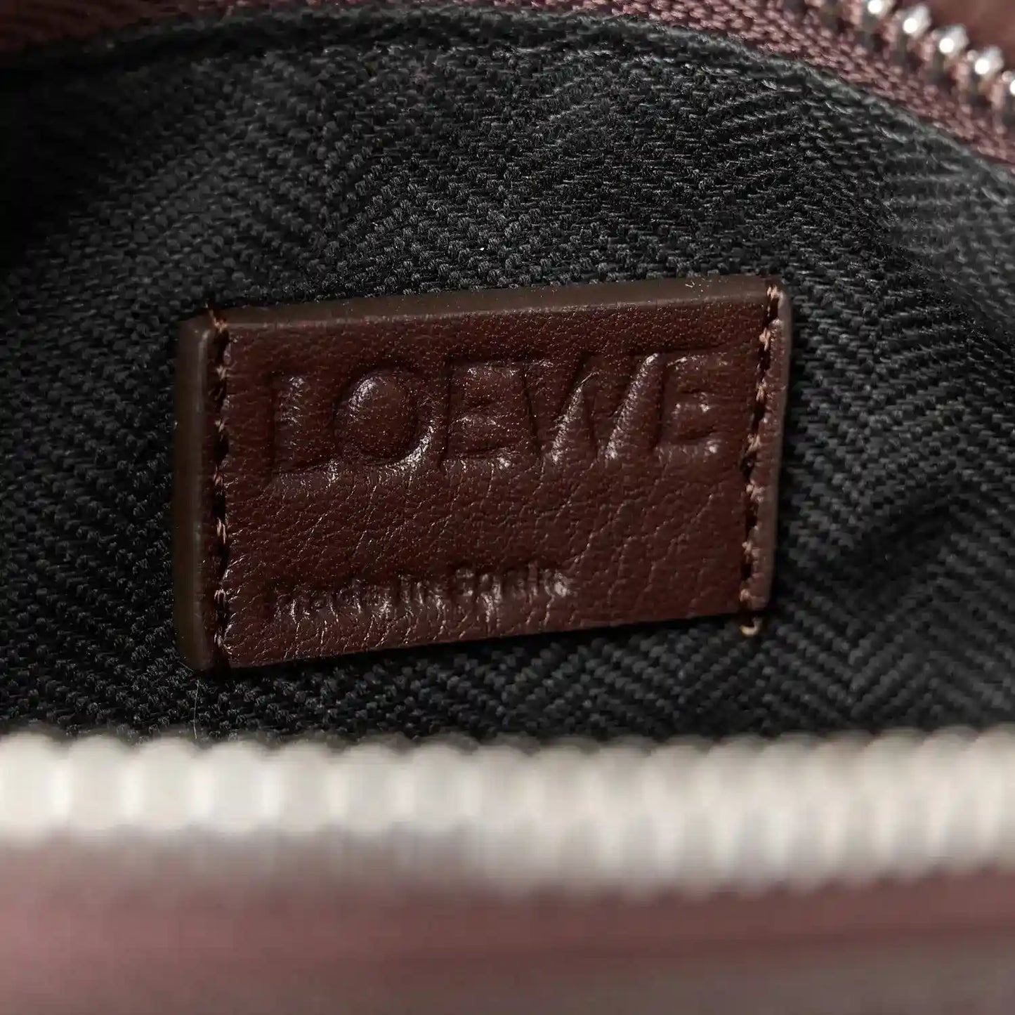 Leather brand patch label on small biker bag strap, dark brown on textured fabric