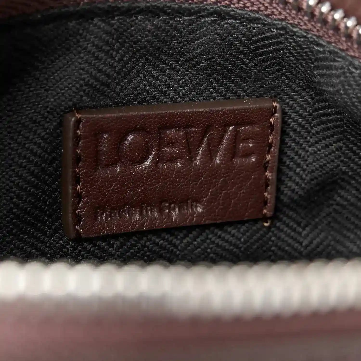 Leather brand patch label on small biker bag strap, dark brown on textured fabric