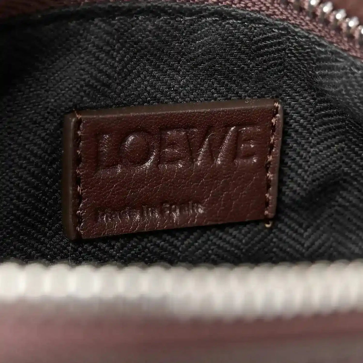 Leather brand patch label on small biker bag strap, dark brown on textured fabric