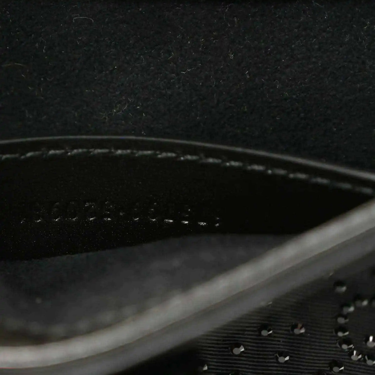 Close-up of black hobo bag seam line and embossed monogram-style texture.