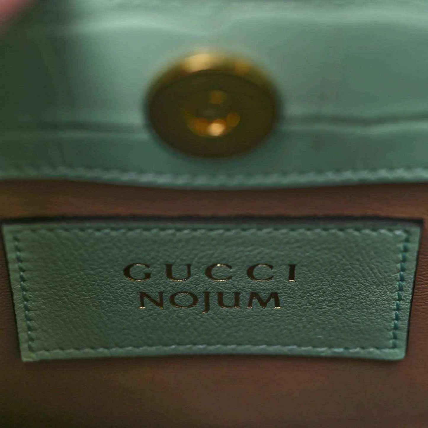 Gucci label on green tote bag lining with gold-tone rivet and stitched border