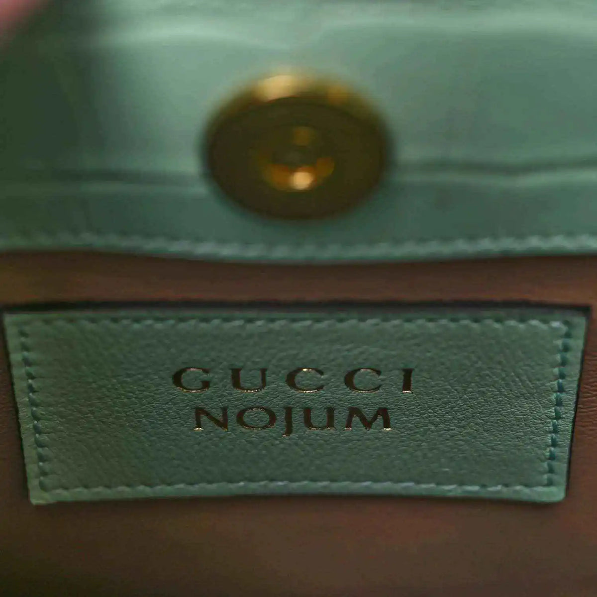 Gucci label on green tote bag lining with gold-tone rivet and stitched border