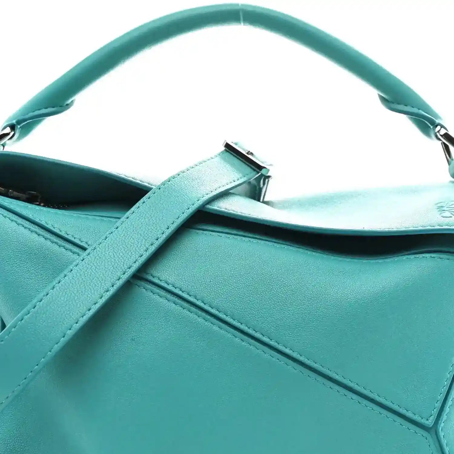Teal-blue small Puzzle bag close-up showing top handle, strap tab, and stitched panel.