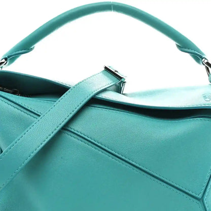 Teal-blue small Puzzle bag close-up showing top handle, strap tab, and stitched panel.