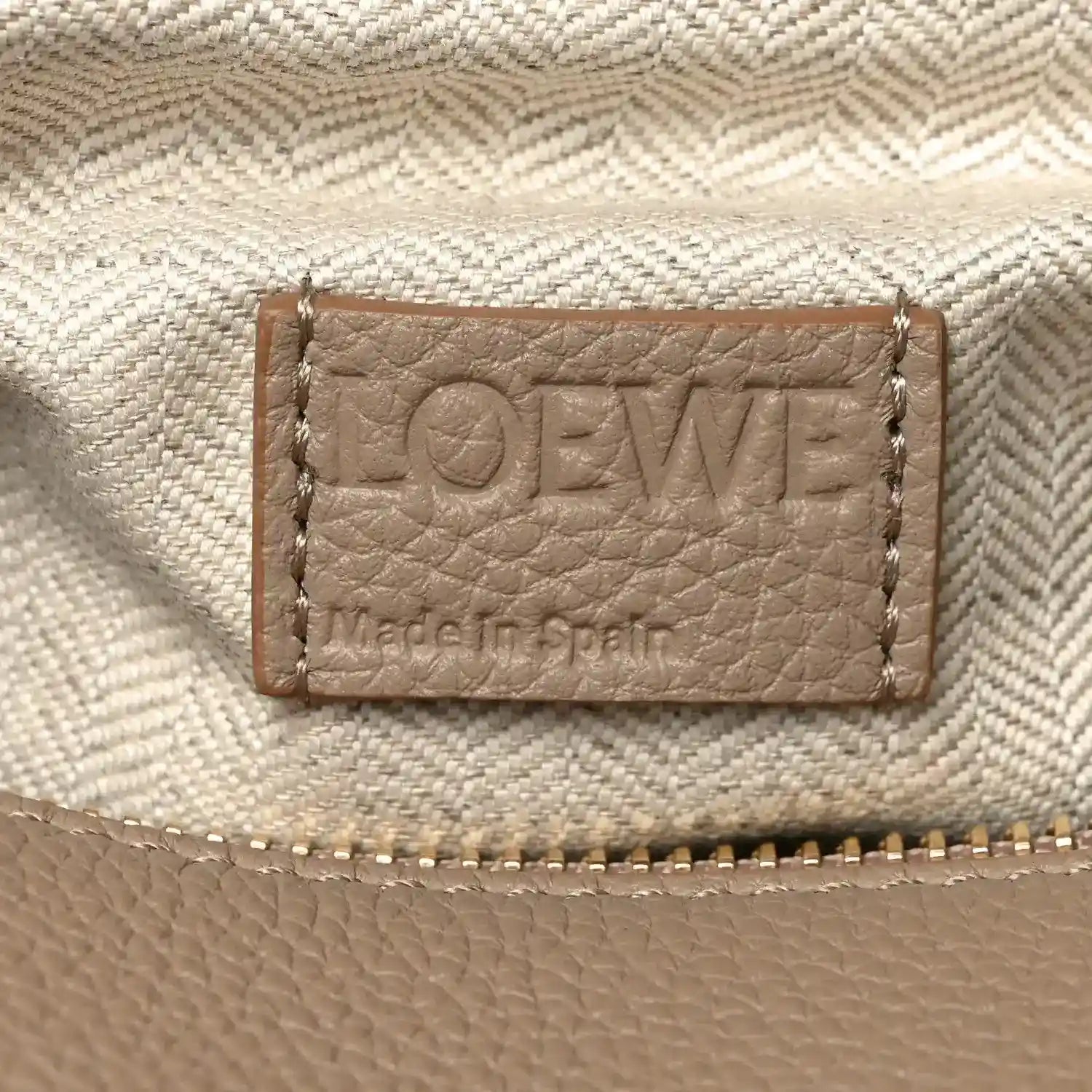 Leather interior label with “LOEWE” text and stitched border on light sand fabric.