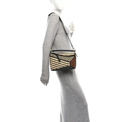 Small raffia puzzle bag worn crossbody with black leather strap and striped weave