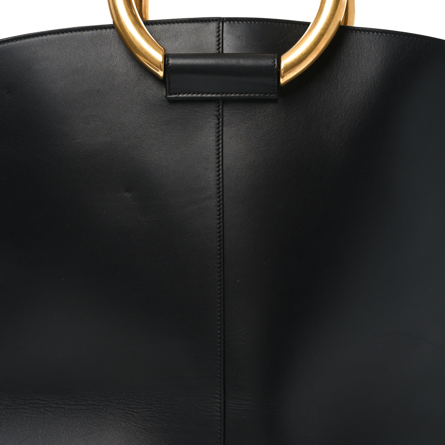 Close-up of black tote top tab and center seam, with gold ring handle