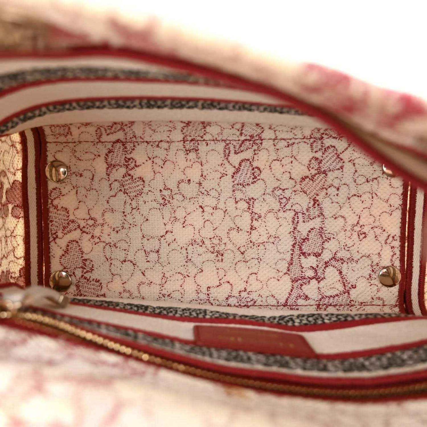 Canvas bag interior closeup with red-and-white stripe trim and gold rivets.