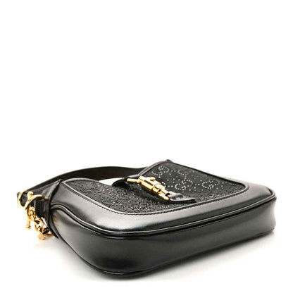 Black hobo bag with gold hardware and a top flap clasp, side view.
