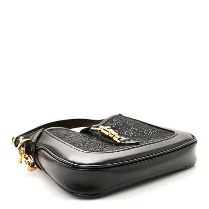 Black hobo bag with gold hardware and a top flap clasp, side view.