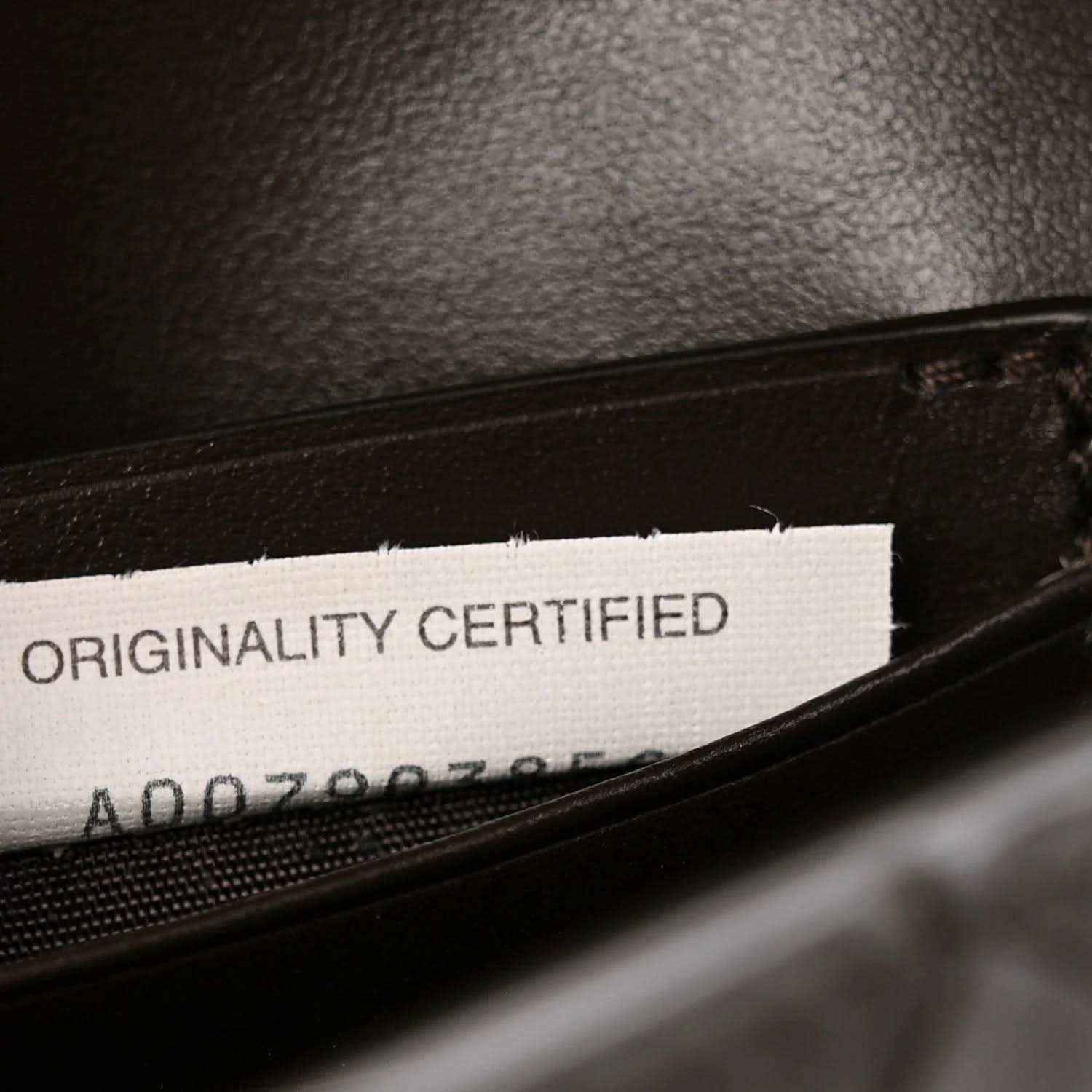 Authenticity label inside leather clutch reading “ORIGINALITY CERTIFIED”