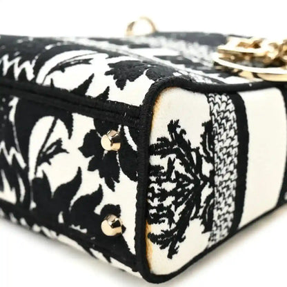 Mini embroidered canvas bag corner detail with black trim, floral panels, and gold studs