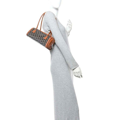 Bonbonnière bag held by a model’s hand over a gray outfit, gray patterned canvas with tan leather
