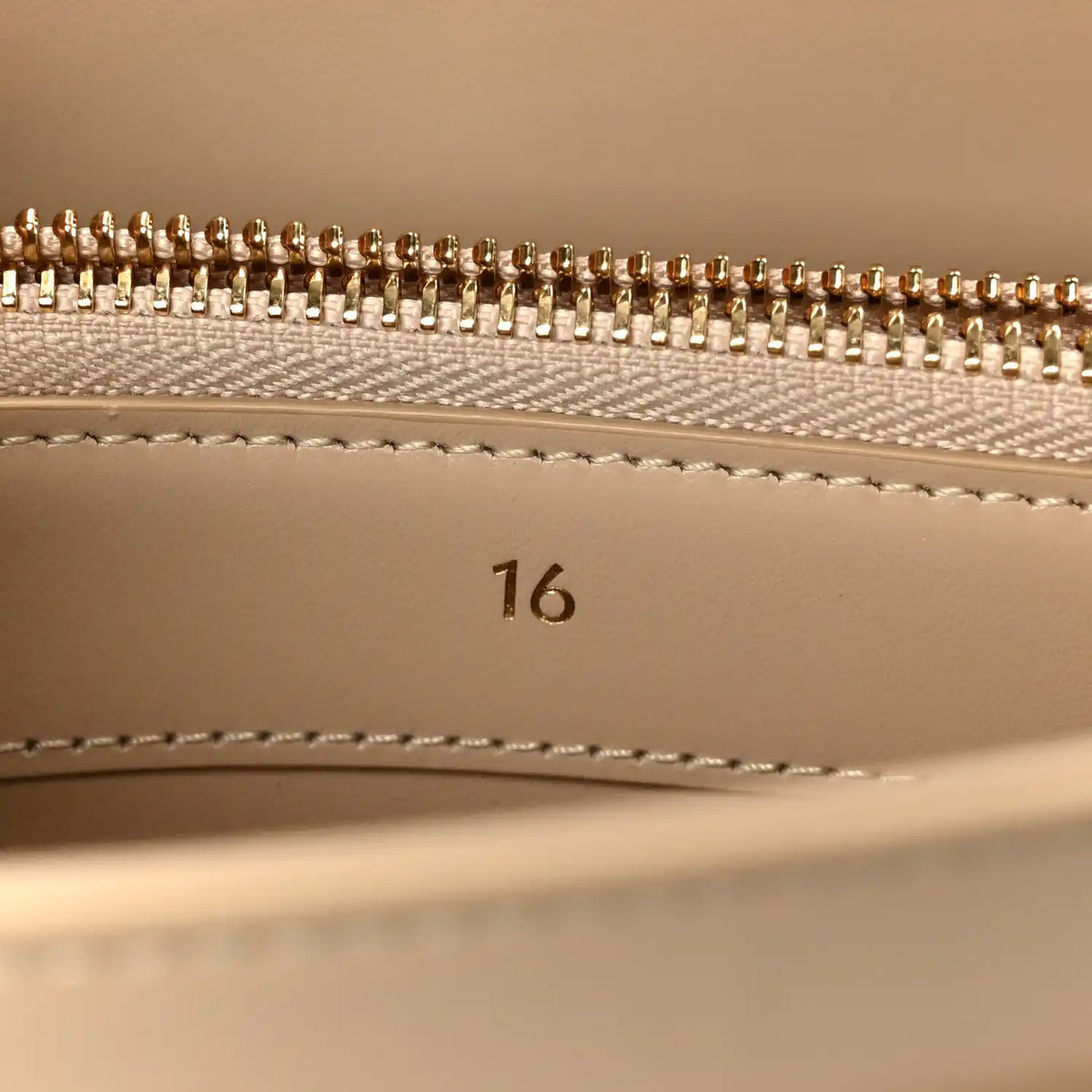 Gold zipper teeth and beige lining with stitched seam inside a small bag