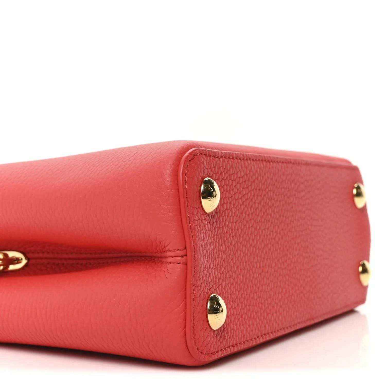 Red leather mini handbag end panel with two gold stud feet and smooth pebbled texture.