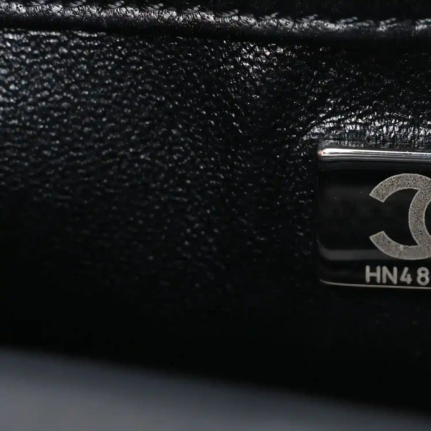 Black satin flap close-up with Chanel emblem hardware and HN48 stamp