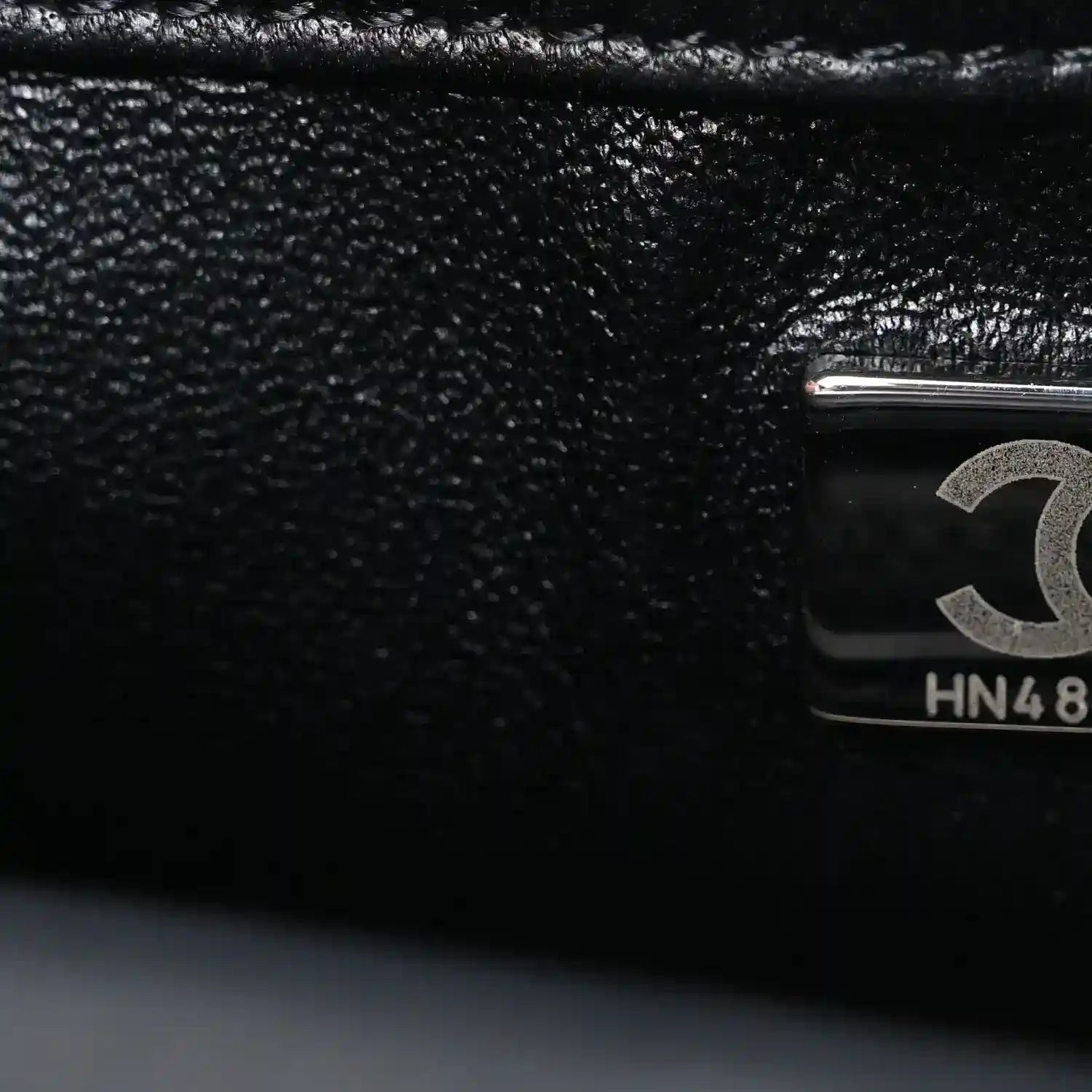 Black satin flap close-up with Chanel emblem hardware and HN48 stamp