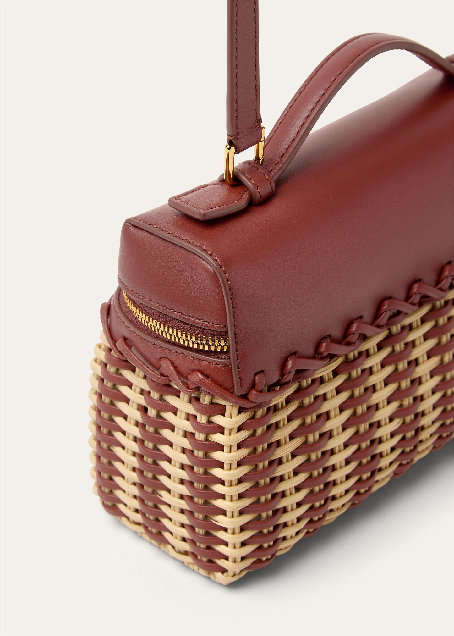 Wicker and calfskin pouch corner with top handle, structured profile and zipped opening.