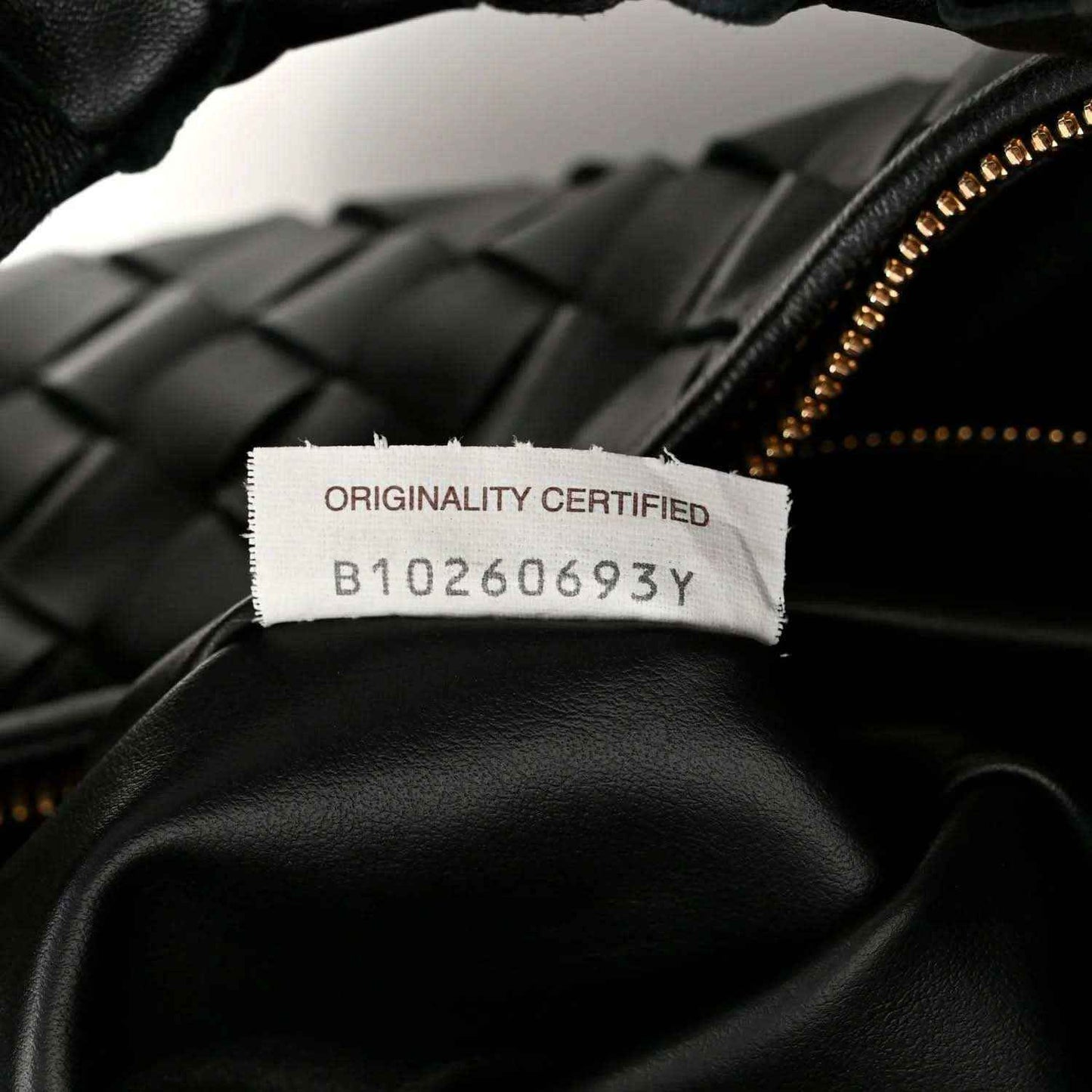 Black leather bag with gold zipper and “ORIGINALITY CERTIFIED” label