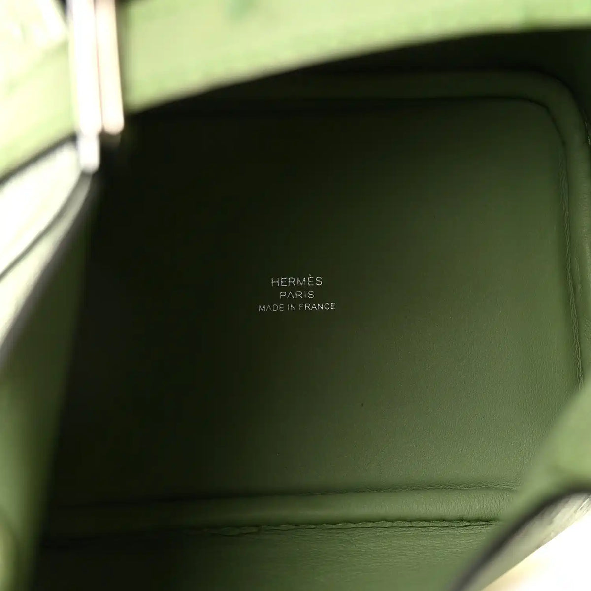 Green leather handbag interior panel with stitched seam and embossed logo text