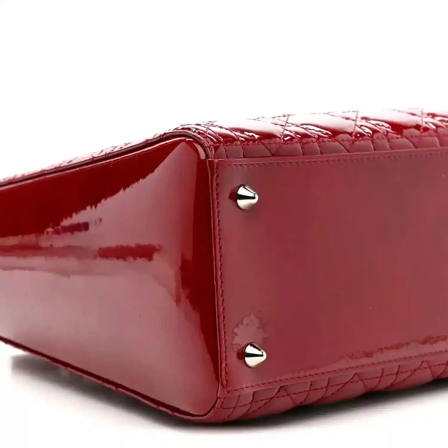 Red patent leather handbag corner with silver studs and quilted cannage texture.