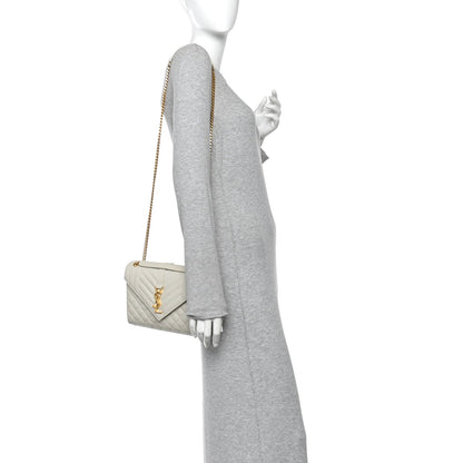 Cream quilted satchel on model, with gold chain shoulder strap and front monogram latch