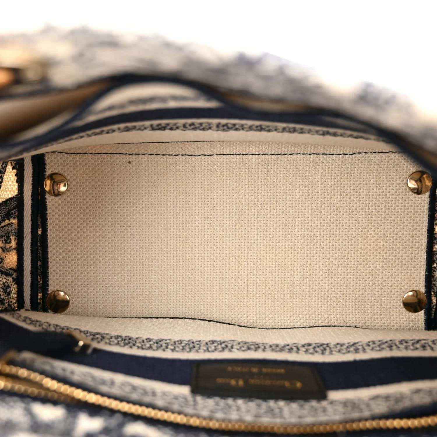 Blue toile de Jouy handbag interior lining and gold snap hardware detail at top edge.