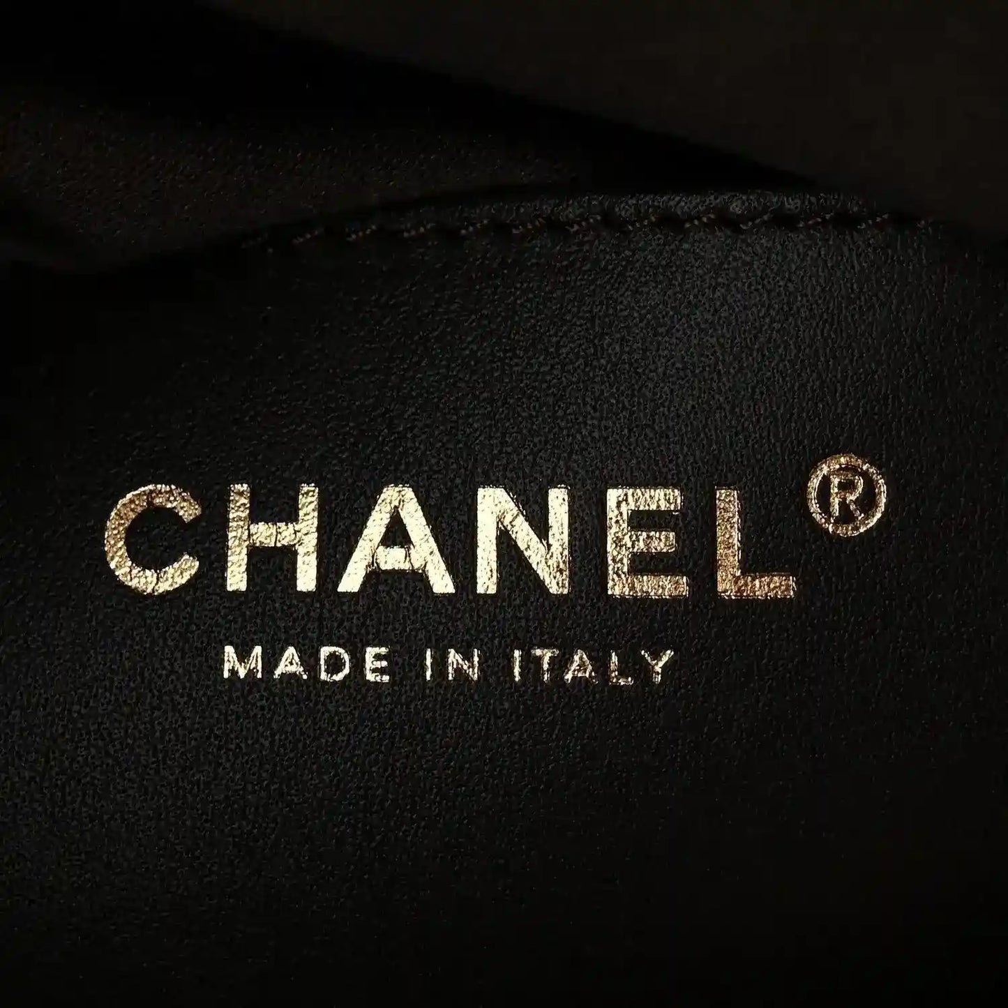 CHANEL logo and MADE IN ITALY on dark fabric with small circular mark