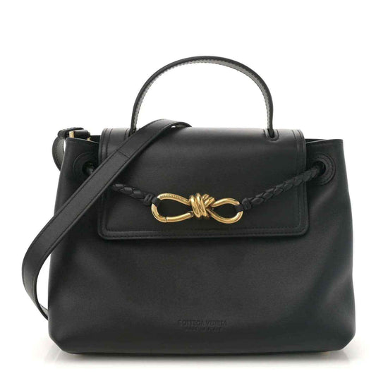 Black leather small shoulder bag with top handle, crossbody strap, and gold bow clasp.