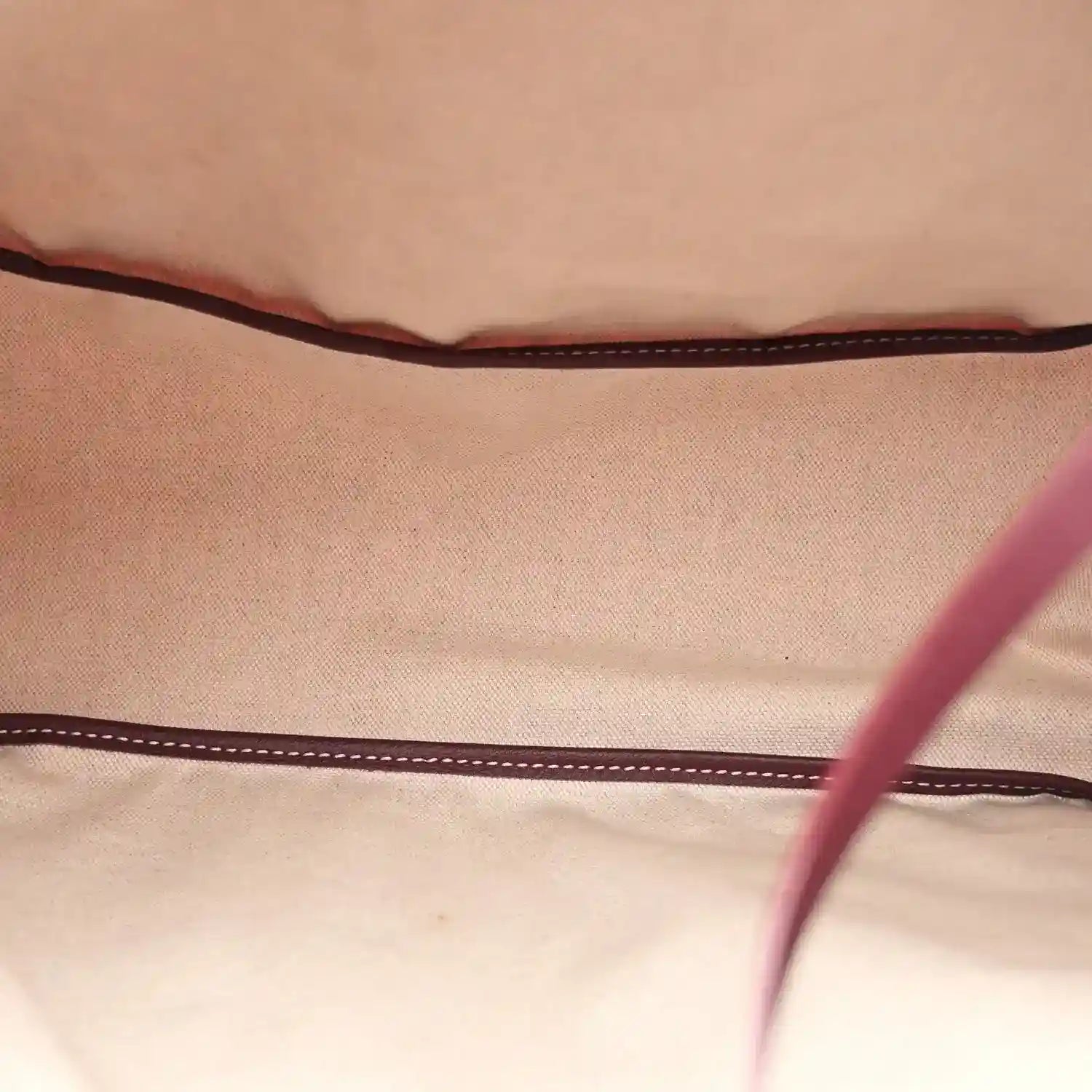 Light beige fabric lining inside burgundy hobo shoulder bag with dark stitched trim