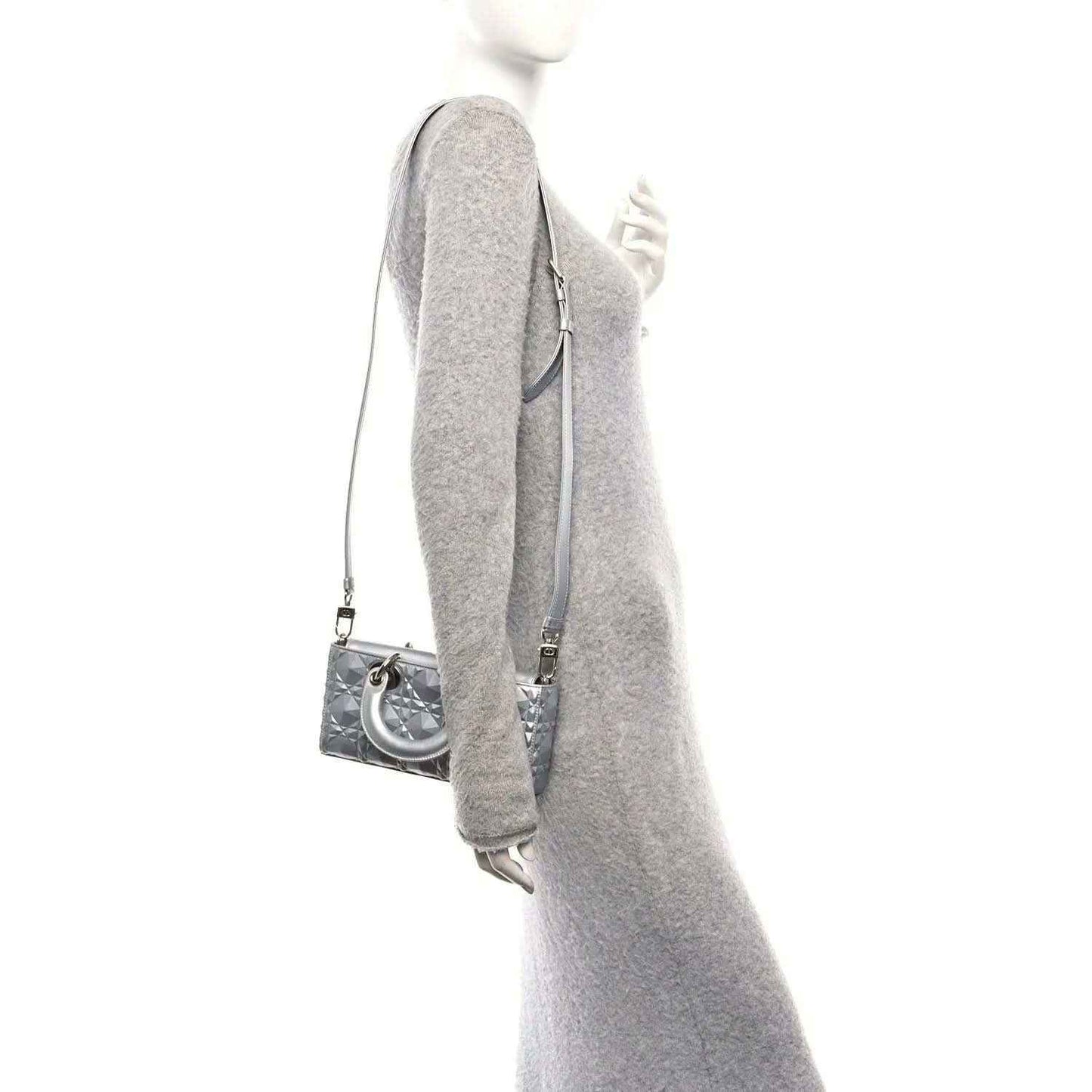 Small metallic silver handbag viewed from the side with shoulder strap and curved handle.