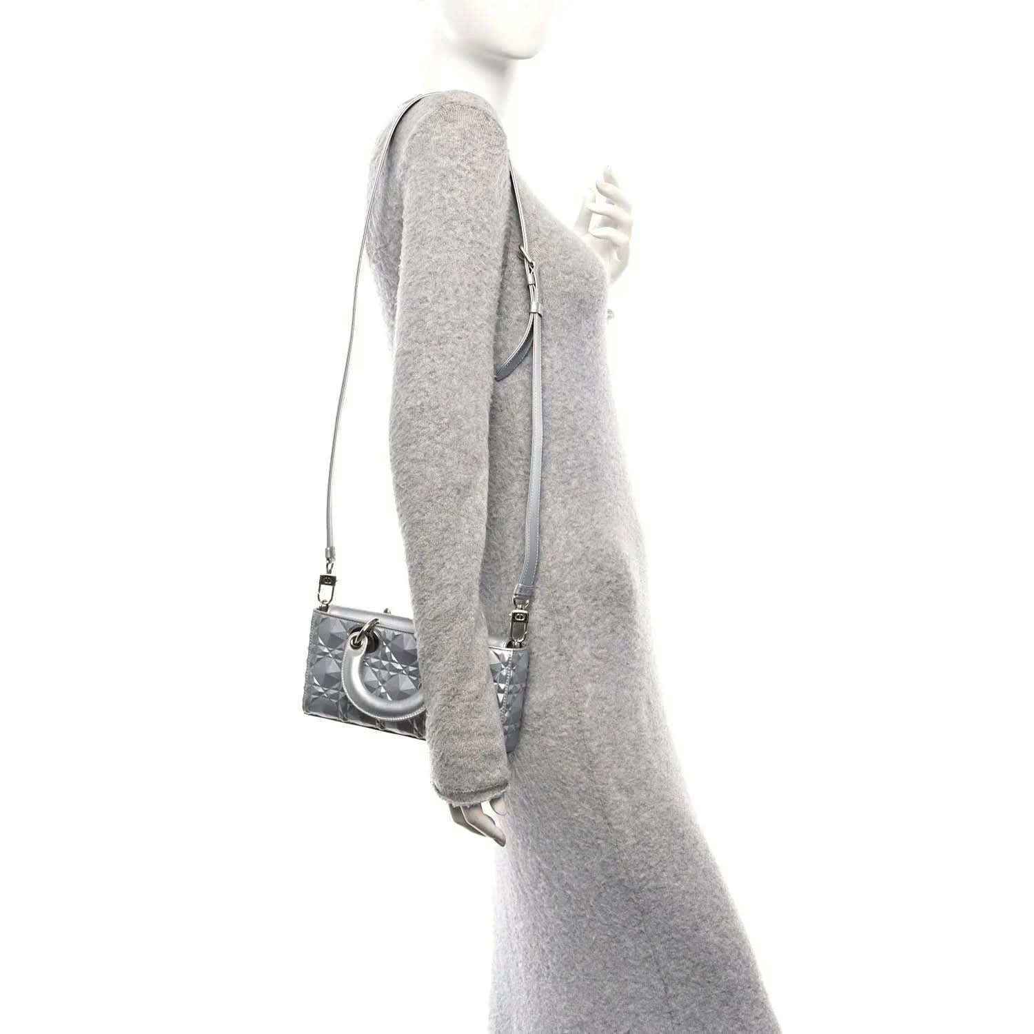 Small metallic silver handbag viewed from the side with shoulder strap and curved handle.