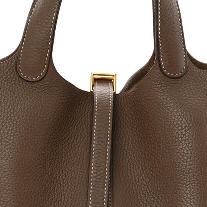 Taupe leather bag close-up of gold clasp on stitched center strap.