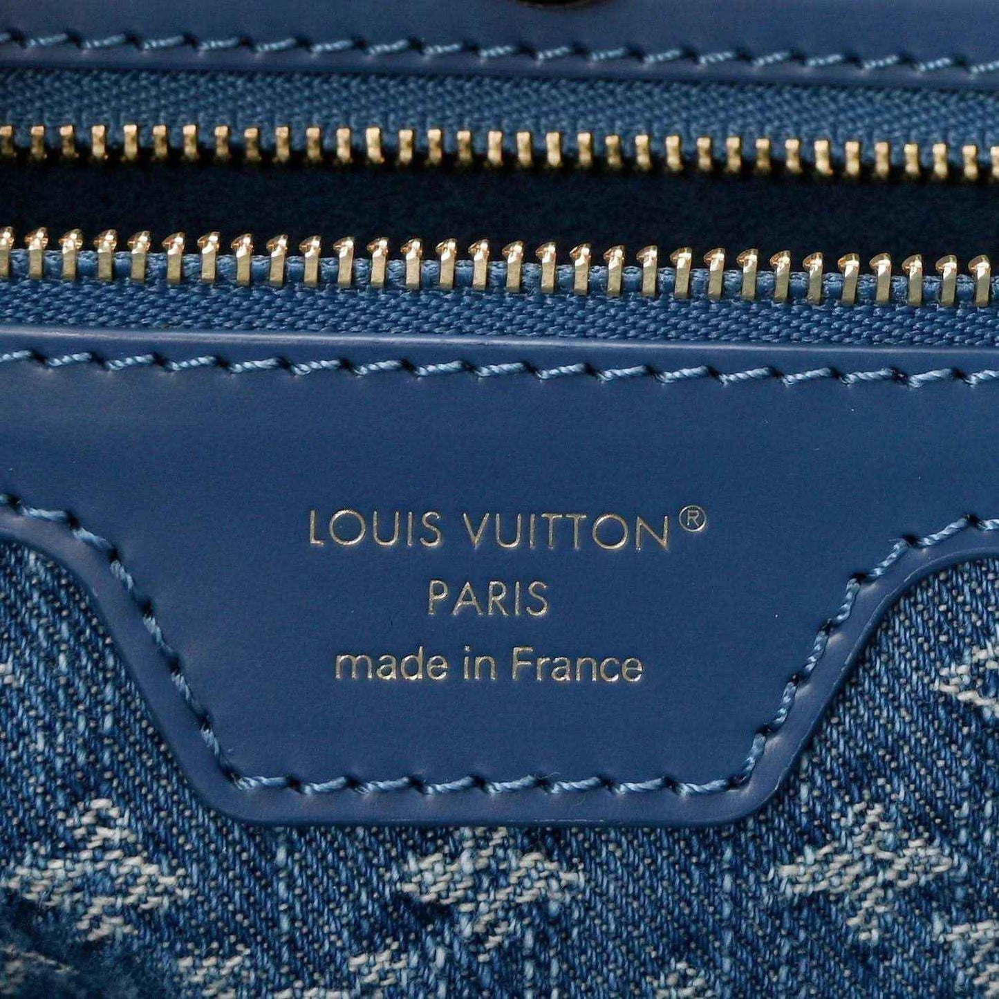 Denim blue leather tote bag close-up of logo label under gold zipper track