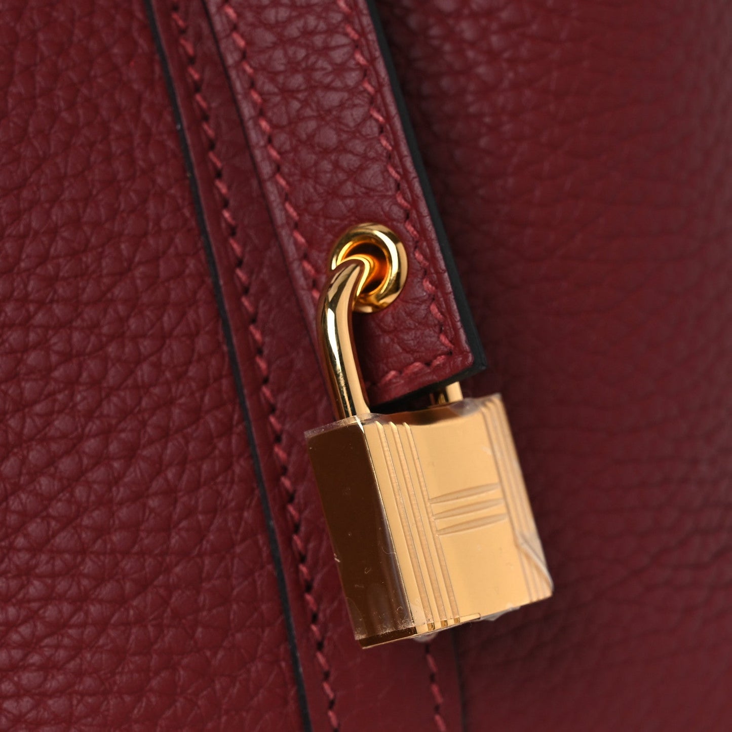 Gold-tone turn-lock clasp with burgundy leather trim and stitched strap