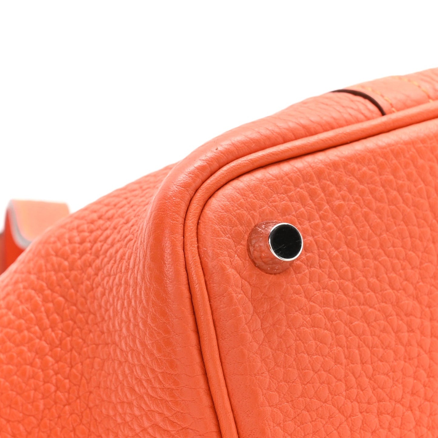 Orange pebbled leather handbag close-up of metal lock stud and grain texture