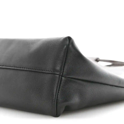 Black leather tote bag side panel with stitched edge and rounded corner.