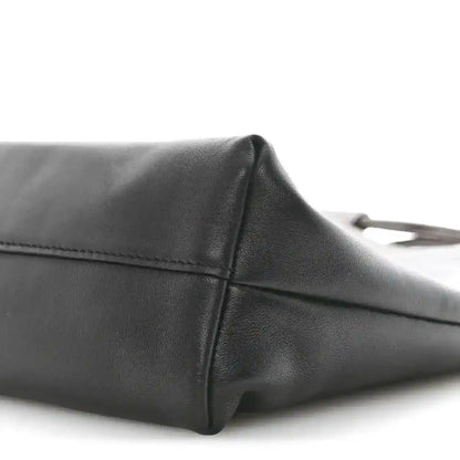 Black leather tote bag side panel with stitched edge and rounded corner.