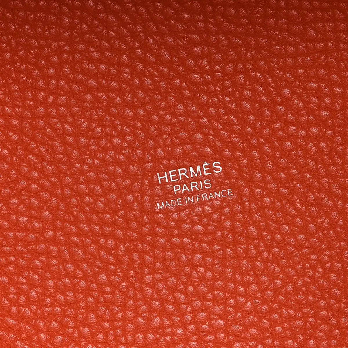 Orange pebbled leather handbag with HERMS PARIS embossed branding label