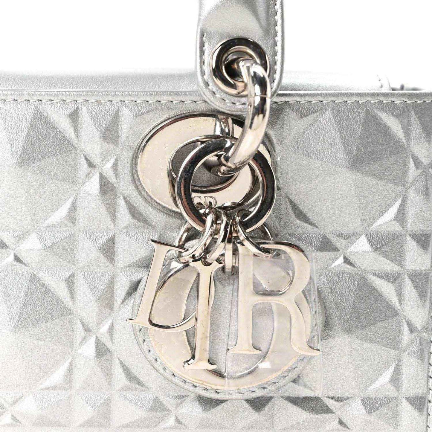 Metal DIOR charm and ring hardware on metallic silver geometric textured handbag.