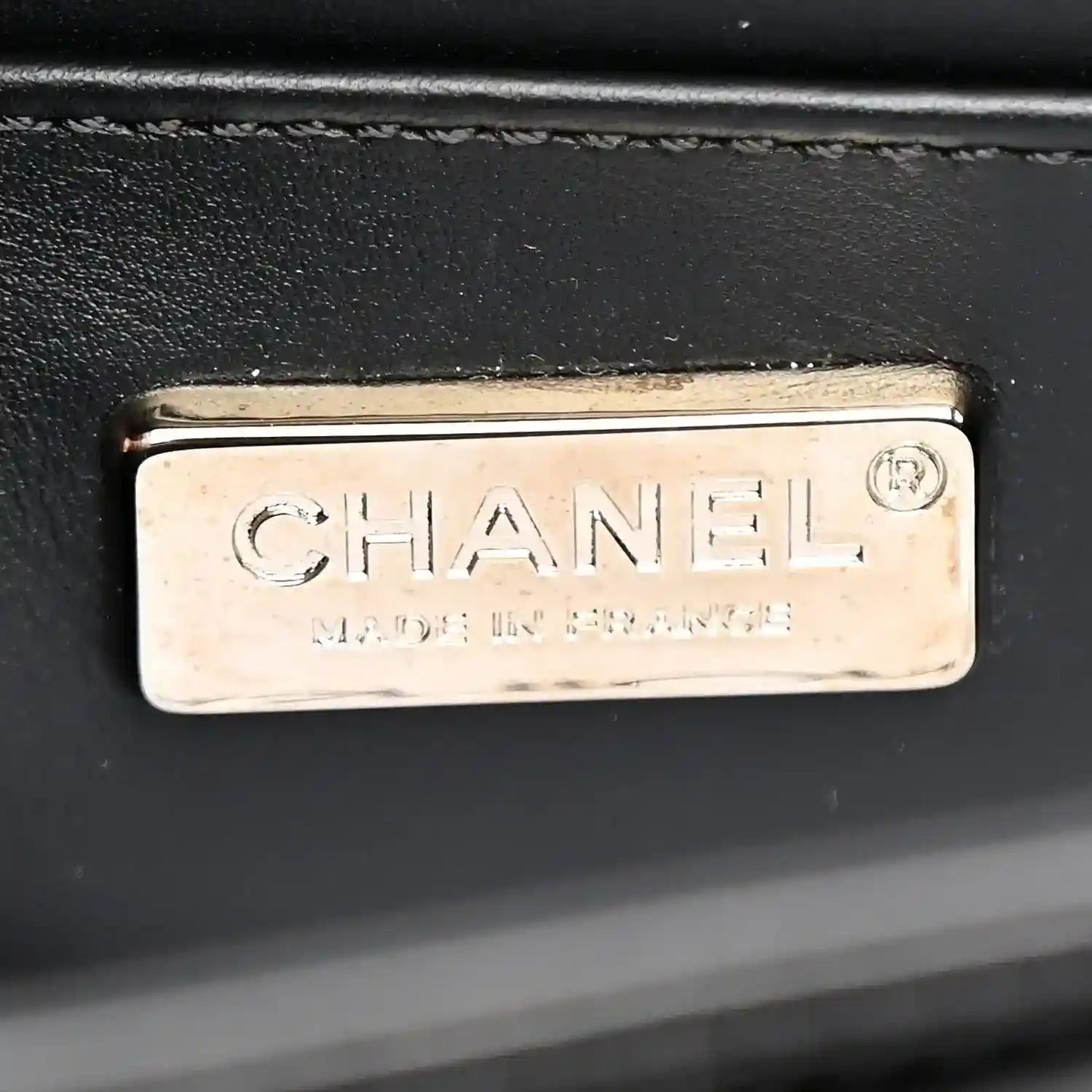 CHANEL metal brand plate on a black bag interior panel.