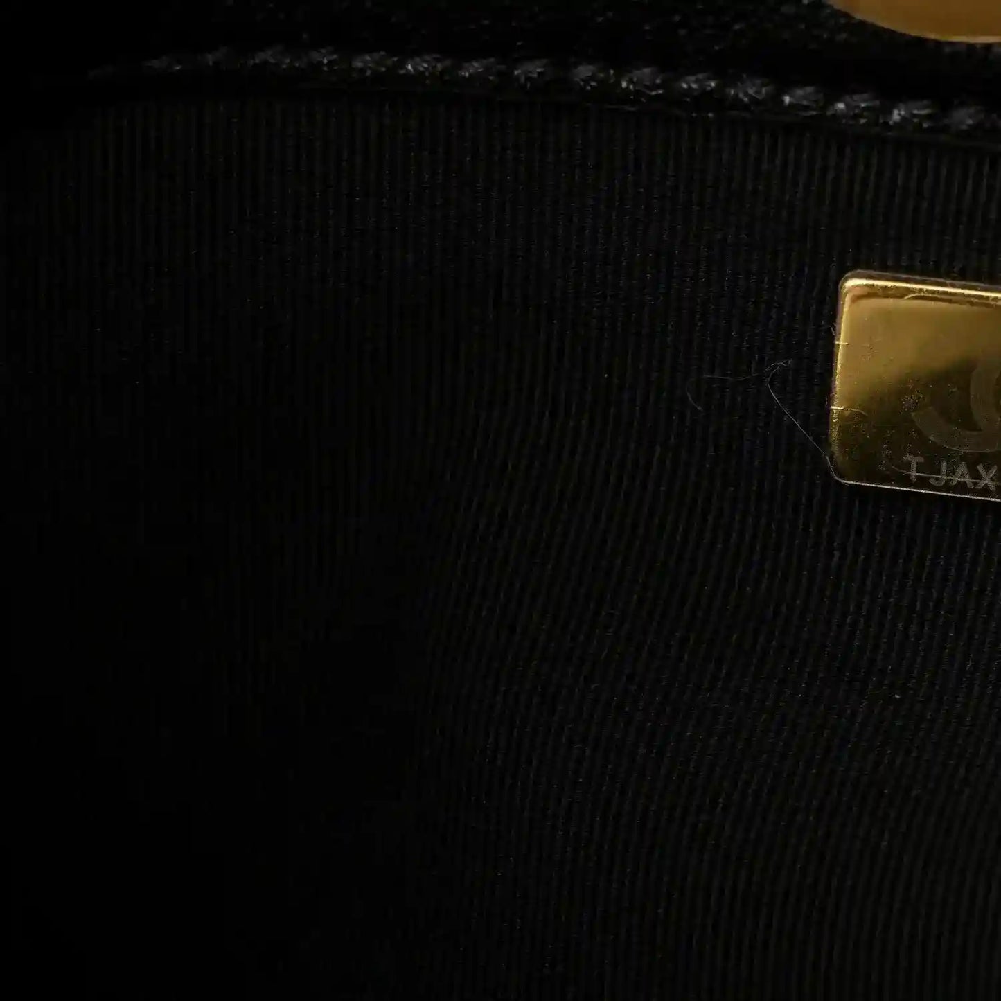 Chanel embossed hardware patch on black lining fabric near a gold edge